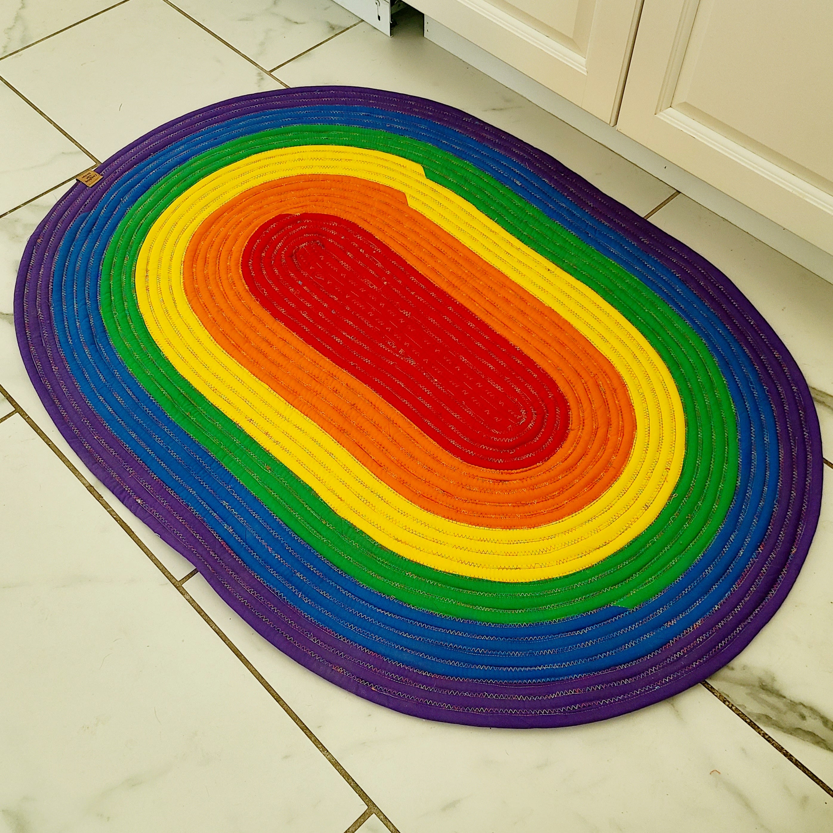 oval rainbow rope rug on white marble with grey veined flooring against white kitchen cabinets base.